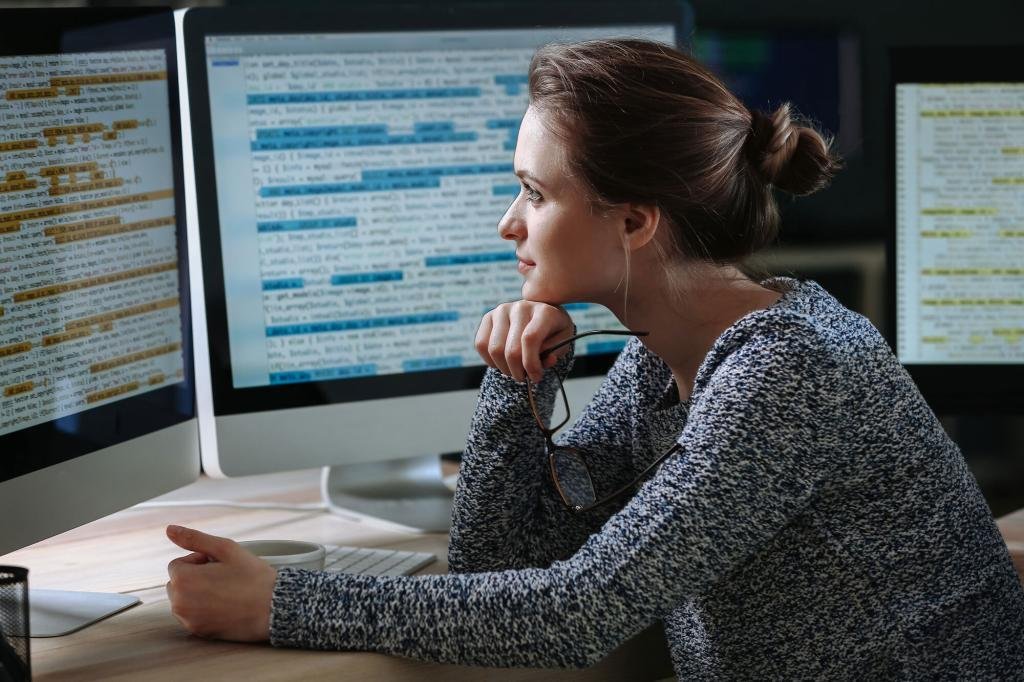 a woman sitting in front of two computer monitors.