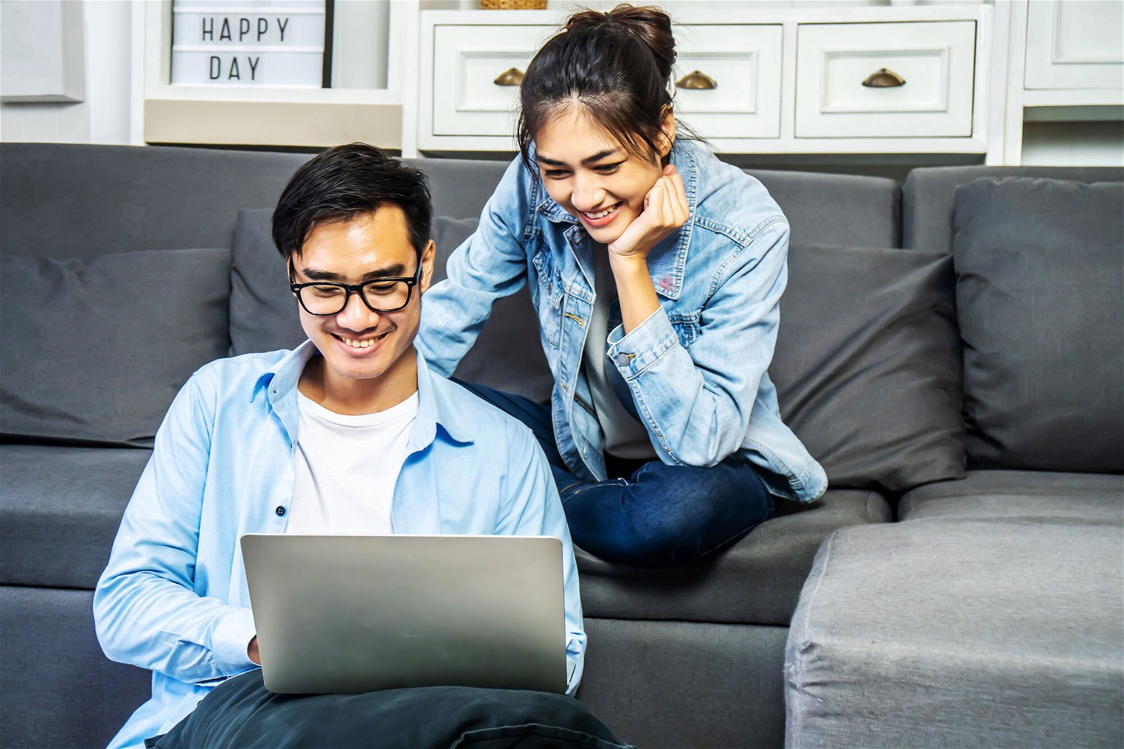 a man and woman sitting on a couch looking at a laptop.